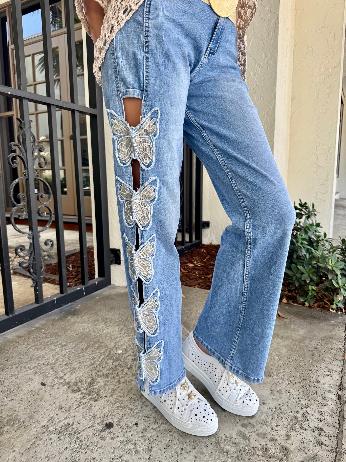 Blue jeans with butterfly patches worn by a person, standing on a concrete surface.