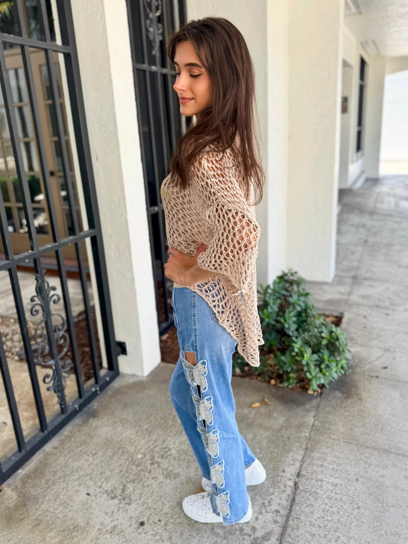 Woman wearing a beige knit sweater and blue jeans standing on a sidewalk.