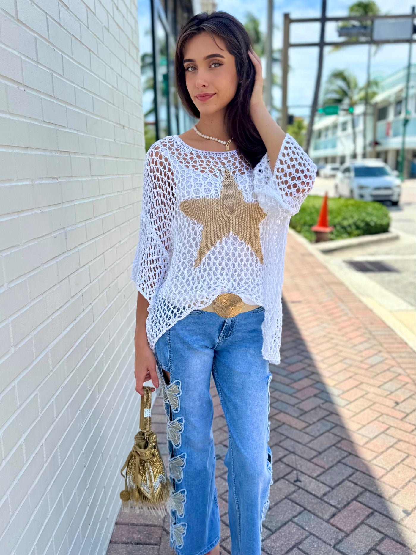 Woman wearing a white star-patterned top and blue jeans on a sidewalk.