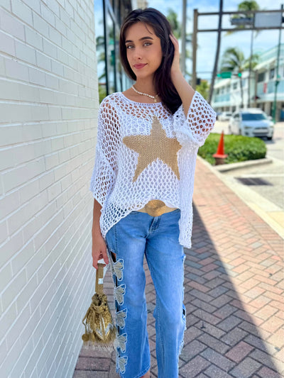 Woman wearing a white star-patterned top and blue jeans on a sidewalk.