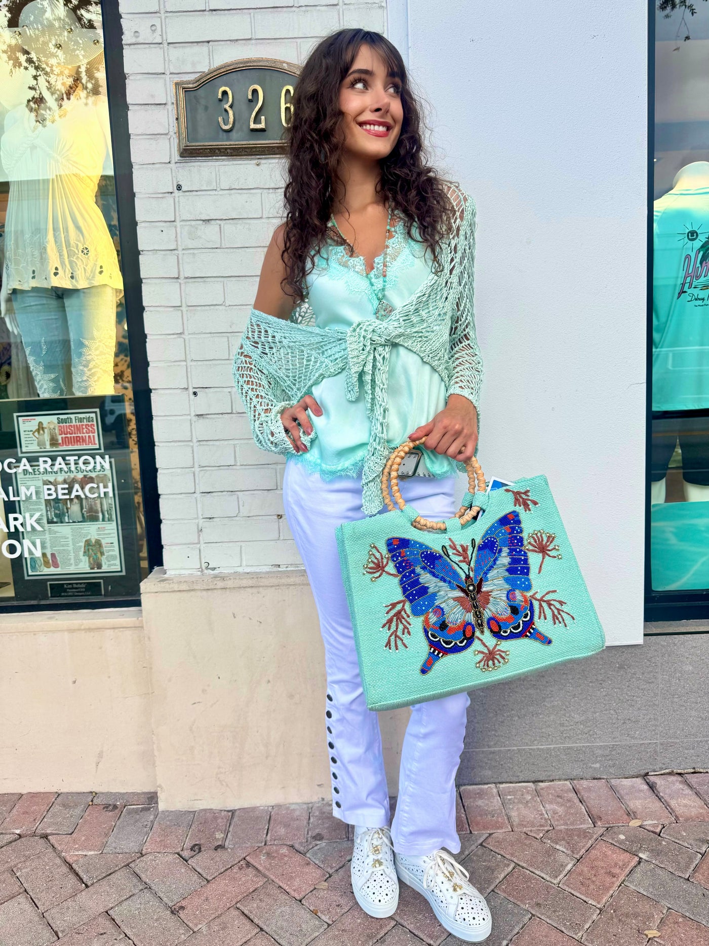 Woman holding a colorful handbag with a butterfly design in front of a store.