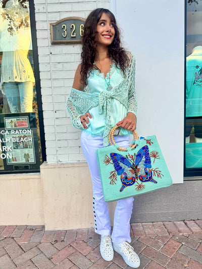 Woman holding a colorful handbag with a butterfly design in front of a store.