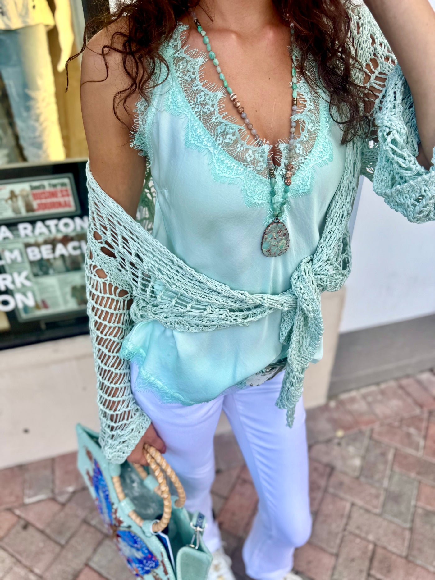 Woman wearing a mint lace top and white pants on a city street.
