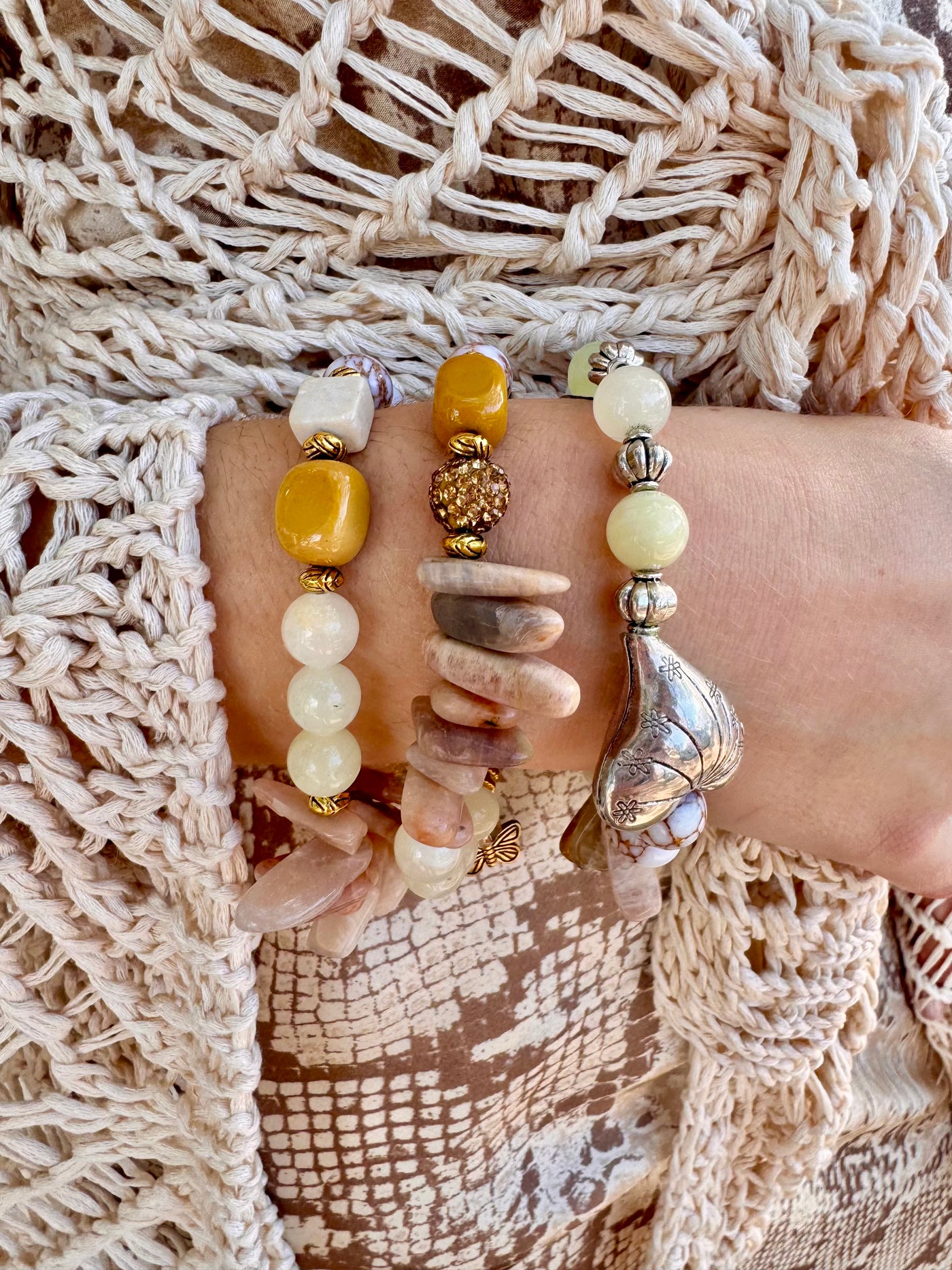 Close-up of a hand wearing multiple beaded bracelets on a textured beige fabric background