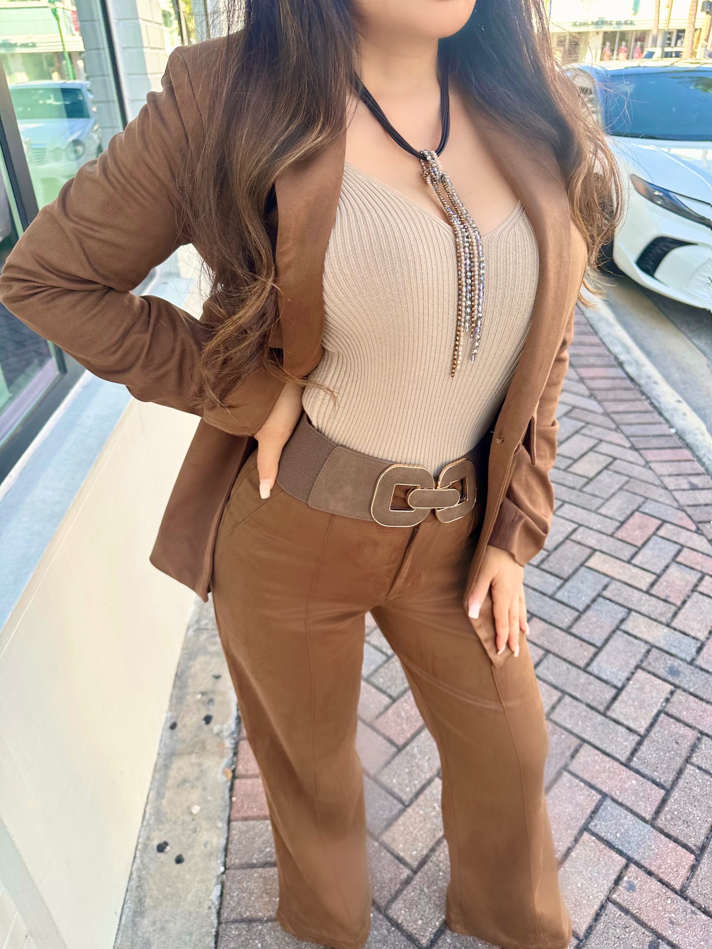 Person wearing a brown blazer, beige top, and pants on a sidewalk.