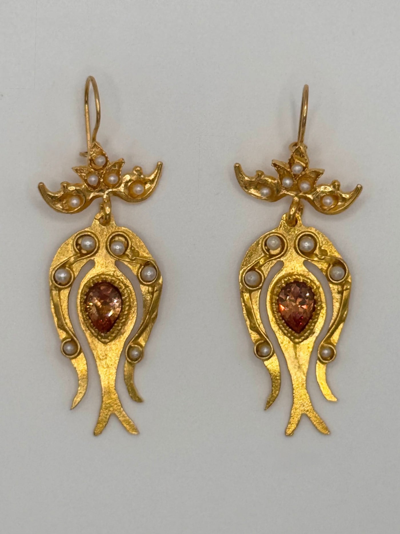 Pair of gold earrings with gemstones and pearls on a gray background