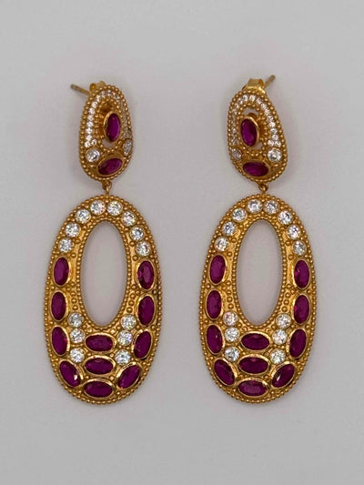 Gold earrings with red gemstones and clear stones on a gray background