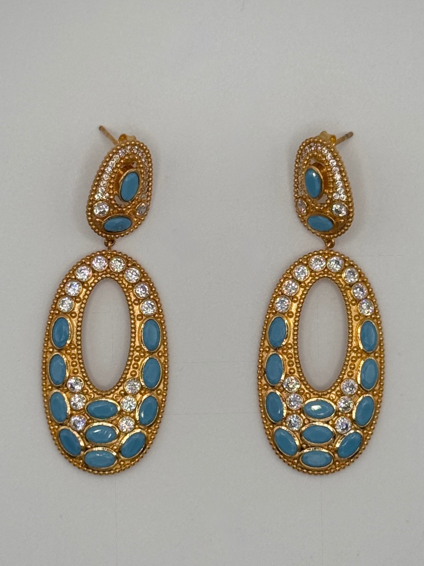 Gold earrings with blue stones and clear gemstones on a gray background
