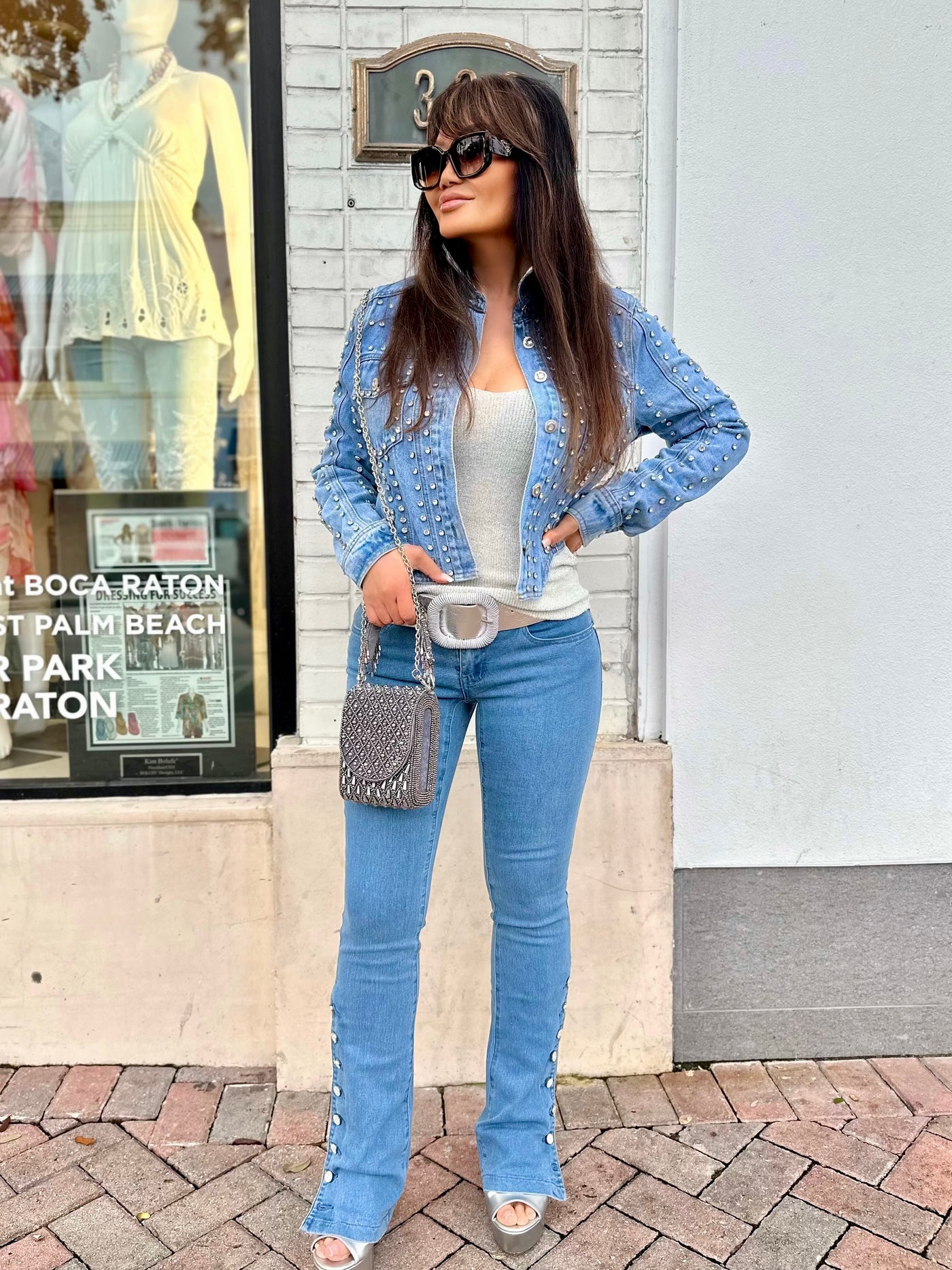 Woman in a blue studded jacket and jeans standing on a sidewalk.