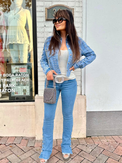 Woman in a blue studded jacket and jeans standing on a sidewalk.